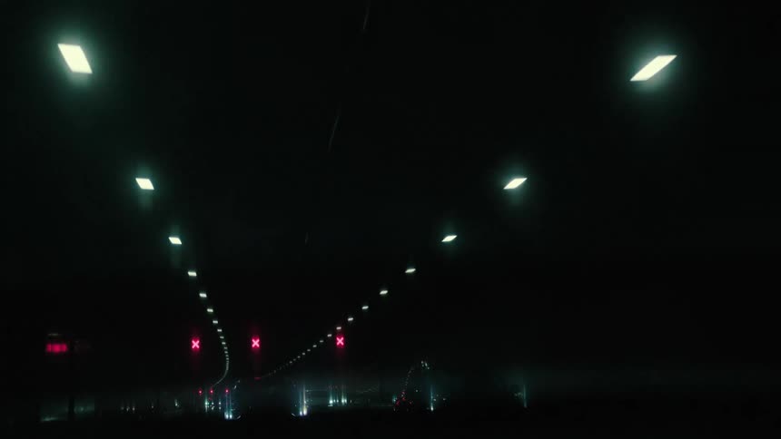 POV shot of driving through a dark highway tunnel at night with illuminated red X signs overhead