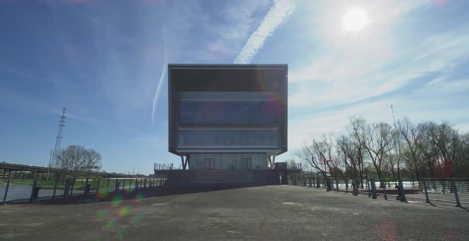 A modern, symmetrical cube-shaped building stands proudly on an empty riverside plaza on a bright and sunny day