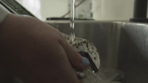 A person's hands hold a rusty wrench under a stream of running water in a sink in slow motion
