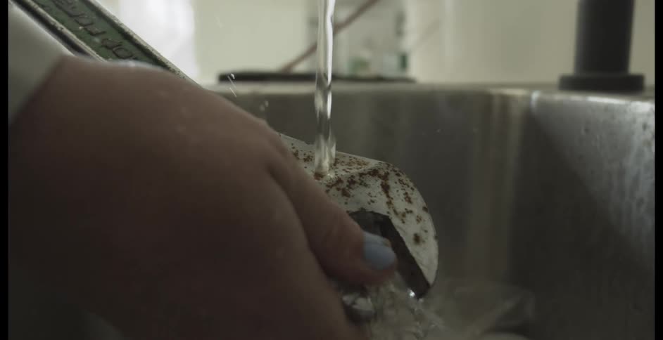 A person's hands hold a rusty wrench under a stream of running water in a sink in slow motion