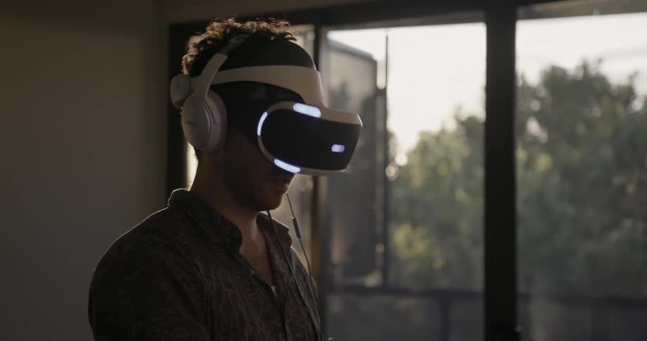 A man wearing a vr headset looks around and raises his hand