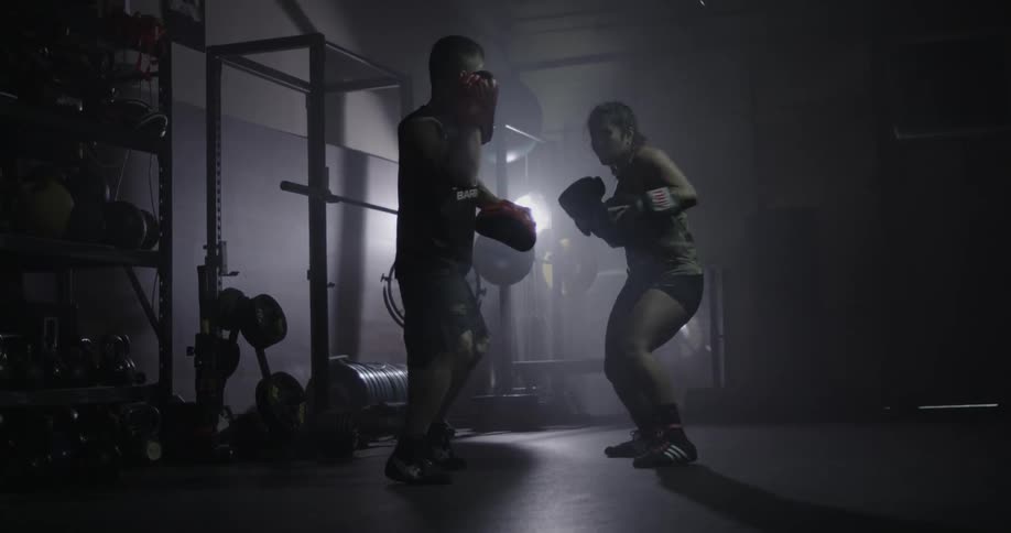 Man and woman practice boxing in a dimly lit gym