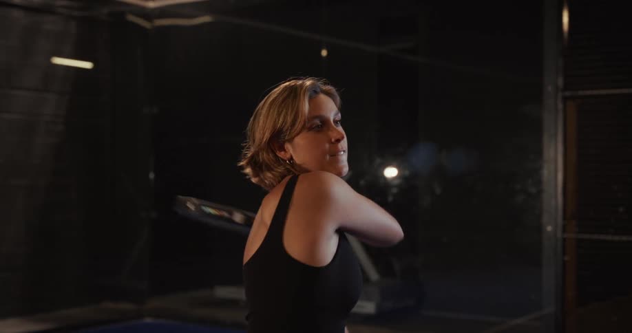 Slow motion montage of a female athlete playing paddle tennis in a dark indoor court