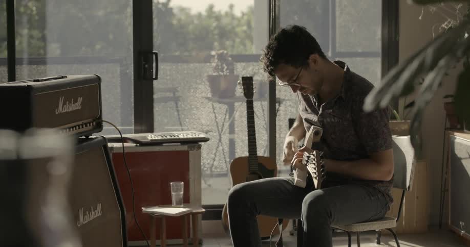 A man sits in a chair playing guitar and composing a song
