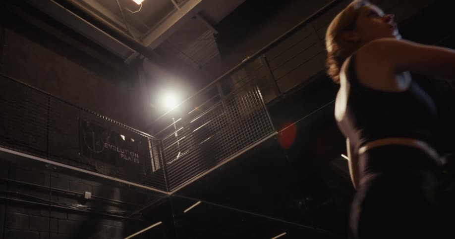 A woman triumphantly raises her padel racket in a dramatically lit indoor court in slow motion