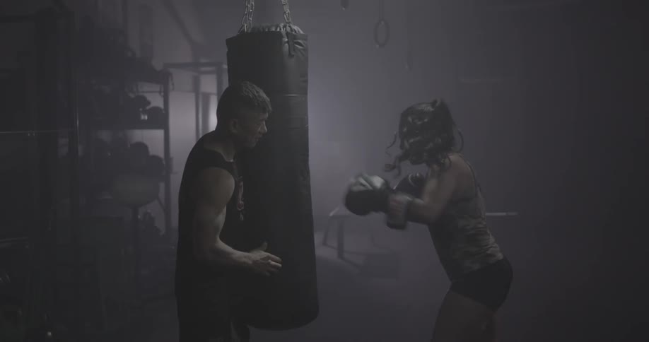 A man is holding a heavy bag as a woman punches it