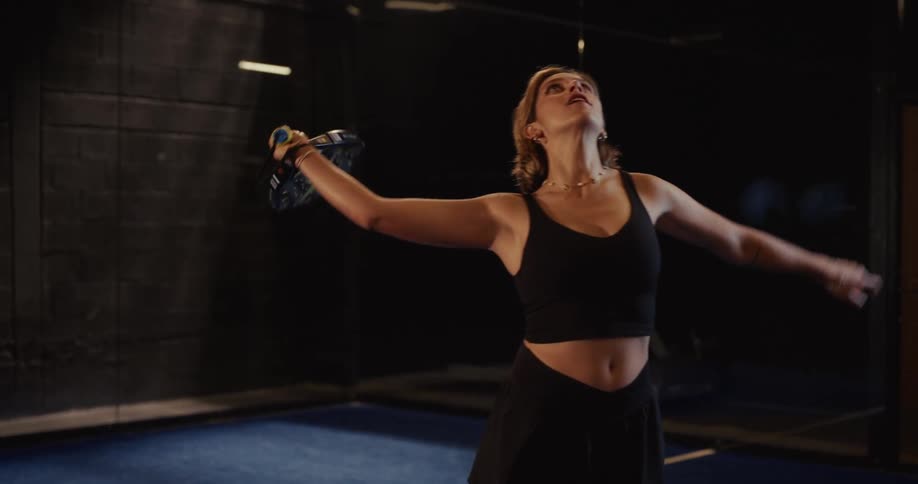 A focused female padel player serves the ball with power in a dramatic slow-motion sequence
