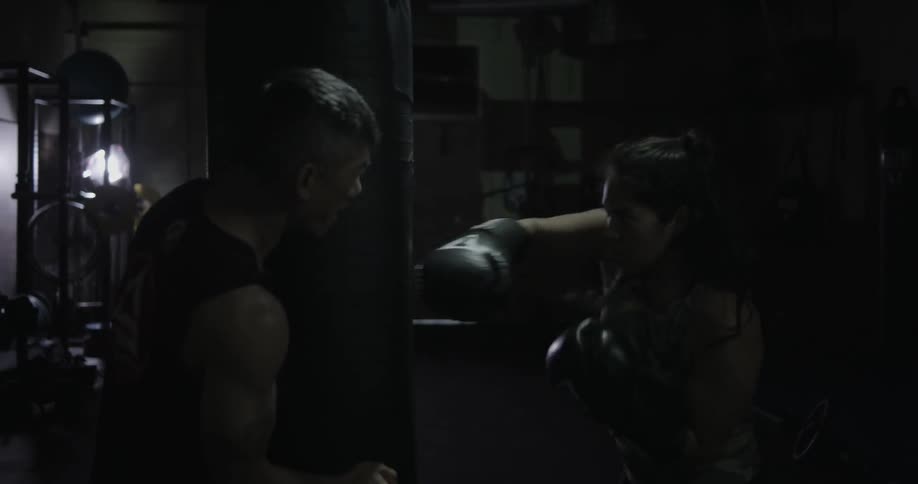 A woman punches a bag fast as a man holds it steady