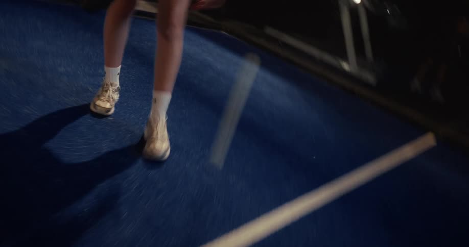 A disorienting, vertigo-inducing close-up of a padel player's feet bouncing a ball on a blue court