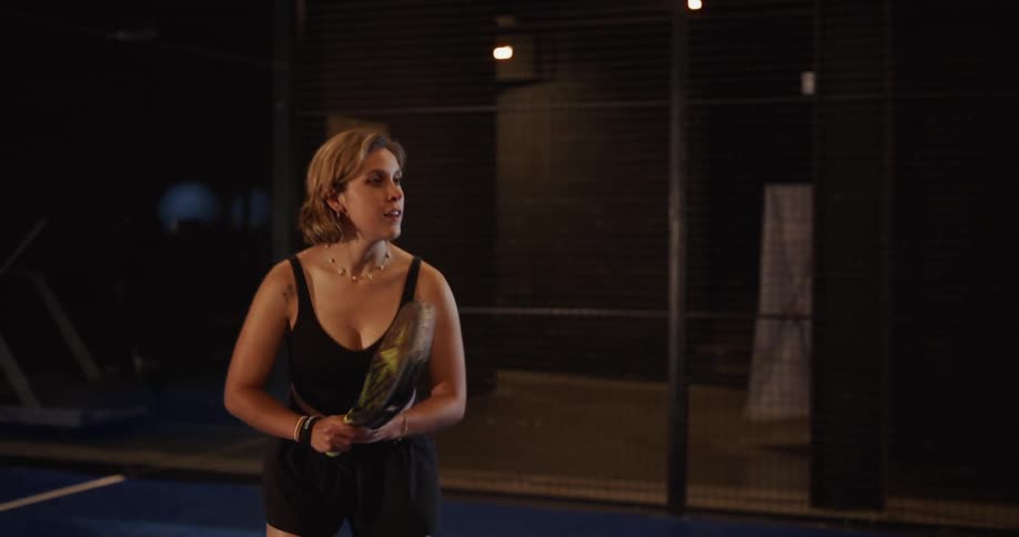 A focused woman hits the ball with her racket in slow motion during a game of padel on an indoor court