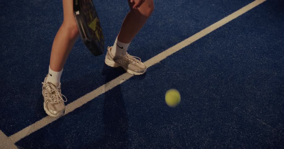 Close-up in slow motion of a female padel player's feet bouncing a ball on a blue court