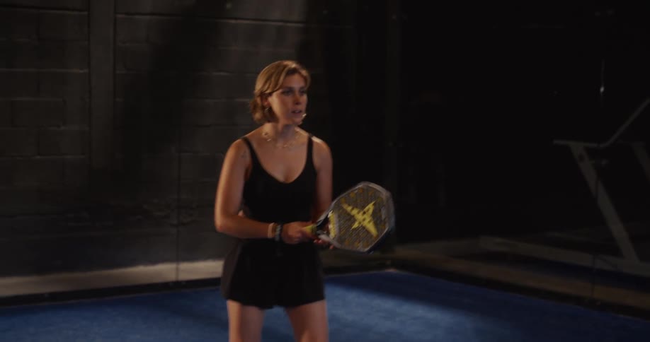 A female athlete in black sportswear practices her swings during a padel tennis training session on a blue indoor court