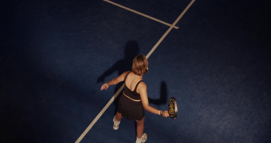 Top-down view of a female padel player executing a powerful serve in slow motion on a blue court