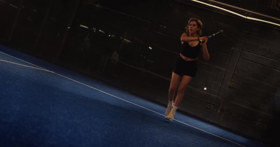 A focused female athlete hits a forehand shot in slow motion during an intense game of padel tennis on a blue indoor court