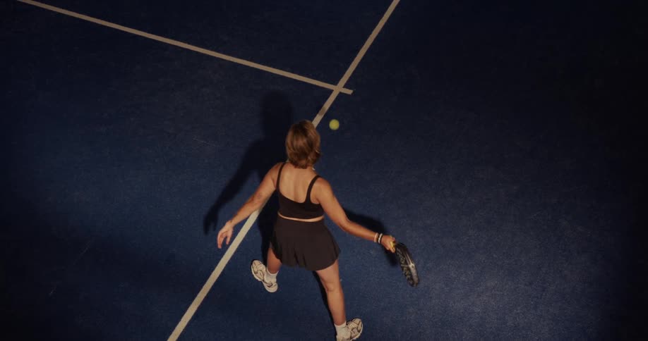 High-angle slow-motion view of a female padel player practicing her serve on a blue court