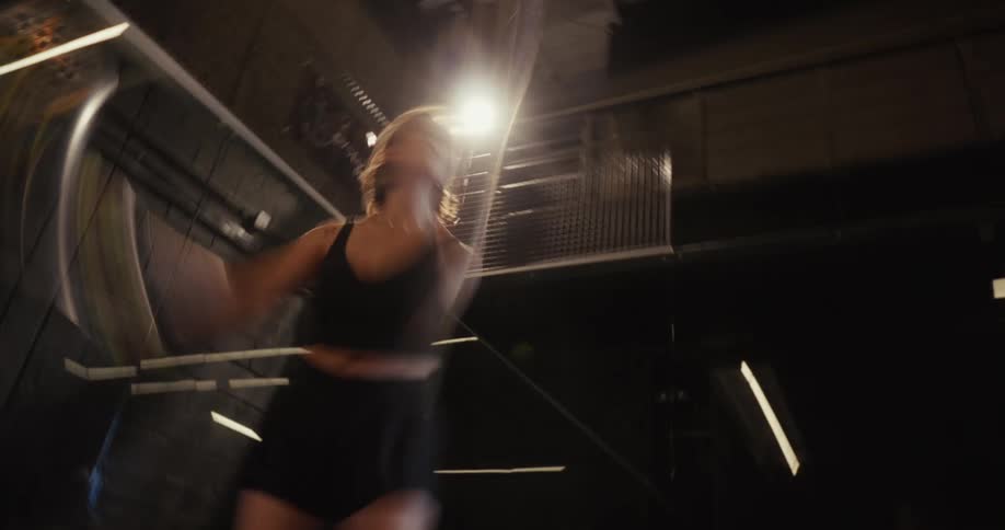 A low-angle, slow-shutter shot captures a woman hitting a powerful overhead smash during a padel match on an indoor court