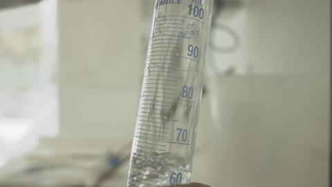 A clear, bubbling liquid is slowly poured into a graduated cylinder, filling it up in a laboratory setting