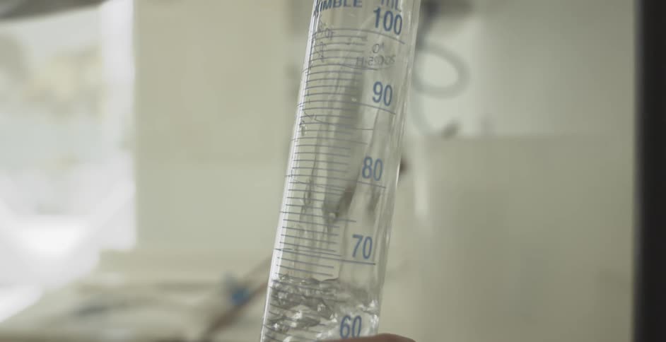 A clear, bubbling liquid is slowly poured into a graduated cylinder, filling it up in a laboratory setting