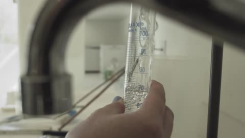 Slow-motion close-up of a lab technician carefully filling a graduated cylinder with clear liquid from a tap