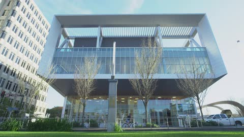 A cyclist rides past the modern glass facade of a contemporary downtown building on a bright sunny day