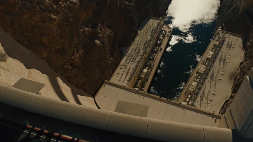 A high-angle perspective tilts down the immense concrete arch of the Hoover Dam, showcasing its scale from the roadway to the Colorado River below