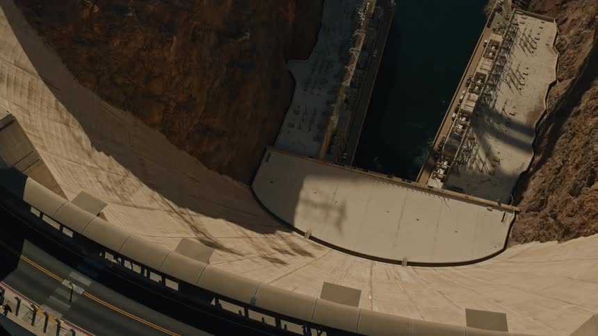 An awe-inspiring top-down view reveals the massive scale of the Hoover Dam, with traffic driving along its crest high above the river