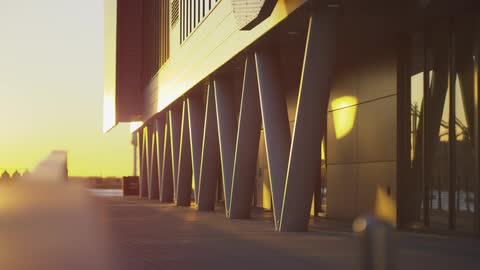 Angled support columns of a modern building are bathed in the warm, golden light of a setting sun