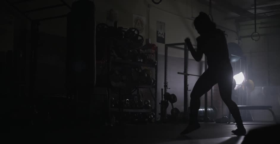 A woman is shadow boxing in a very dark gym alone
