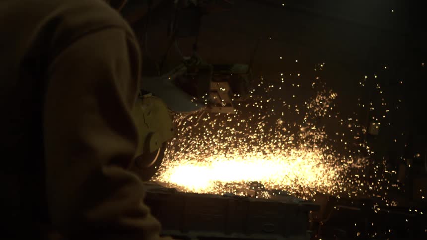 Slow motion shot of a worker using an industrial chop saw, sending a brilliant shower of sparks flying as they cut through a piece of metal in a dark factory