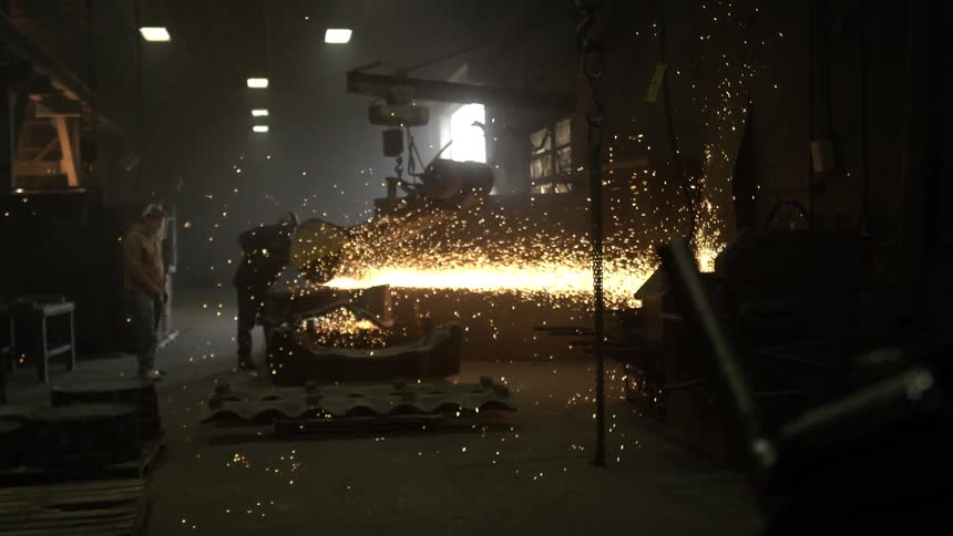 In a dimly lit industrial workshop, a metalworker grinds steel, creating a brilliant shower of glowing sparks in dramatic slow motion