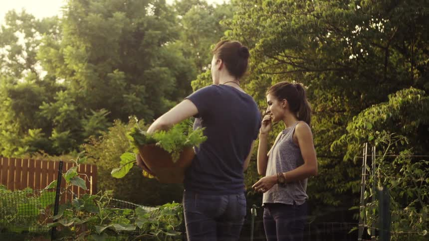Two women talk and eat greens in a garden