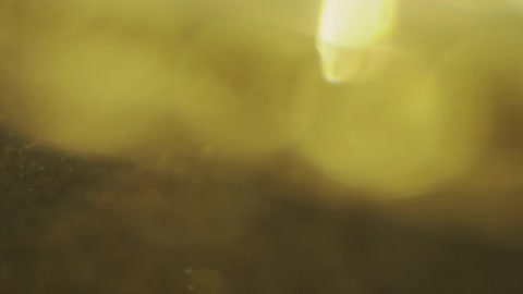 Abstract macro footage shows dark sand and shimmering gold particles moving slowly through a hazy liquid