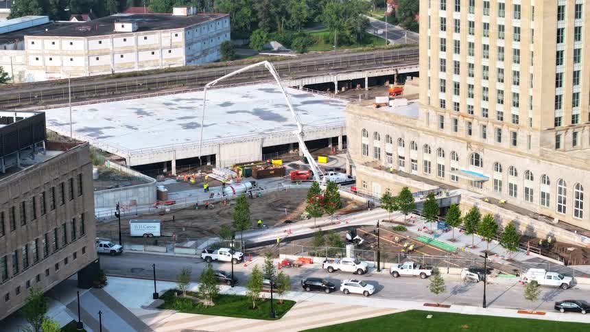 A high-angle timelapse captures a bustling urban construction site where workers and heavy machinery, including a large concrete pump, build a new structure