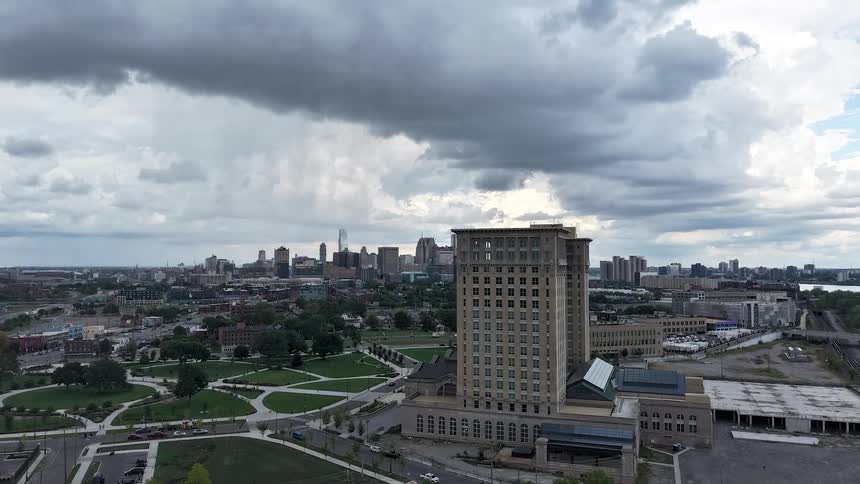 A slow aerial approach to the historic Michigan Central Station, revealing the Detroit city skyline under dramatic storm clouds