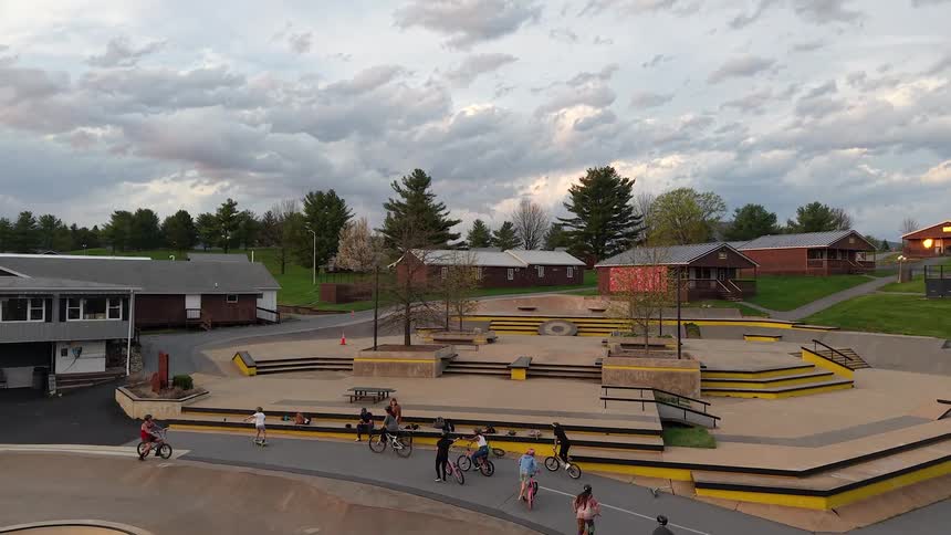 A beautiful golden sunset provides the backdrop for an epic aerial view of a large outdoor BMX and skatepark complex in the countryside