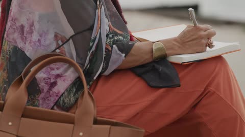 Close up on the hands of a stylish woman as she sits outdoors writing her thoughts in a journal