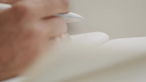 An artistic close-up captures a hand with pink nails turning a blank page and writing in a journal