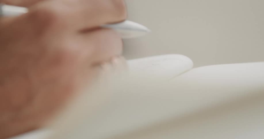 An artistic close-up captures a hand with pink nails turning a blank page and writing in a journal