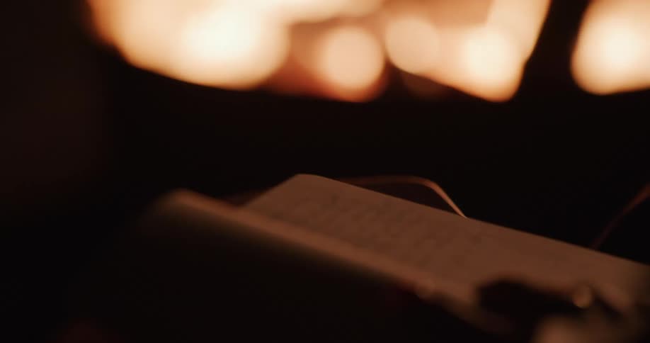 A person's hand writes in a journal with a pen, silhouetted by the warm light of a crackling fire