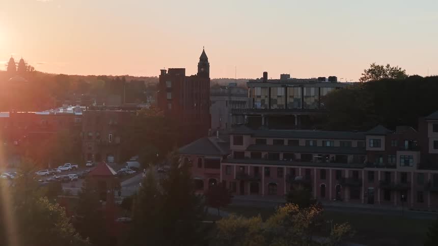 A slow rising aerial view reveals the downtown skyline of a small city during a beautiful golden hour sunset