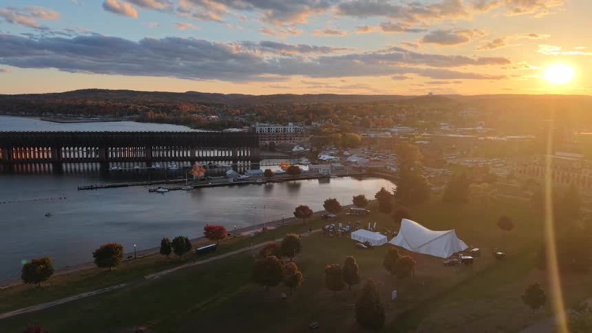A slow aerial pullback reveals a beautiful coastal town with a large ore dock and park during a golden autumn sunset