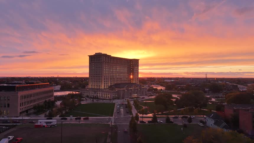 A stunning wide aerial shot captures the beautifully lit Michigan Central Station in Detroit against a fiery and colorful sunrise
