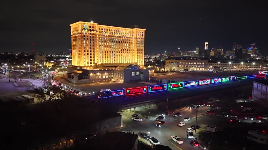Aerial view of the CPKC Holiday Train with festive lights passing the historic Michigan Central Station at night in Detroit
