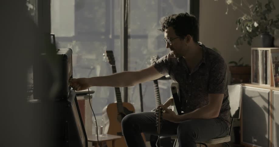 A man plays guitar near a sliding glass door