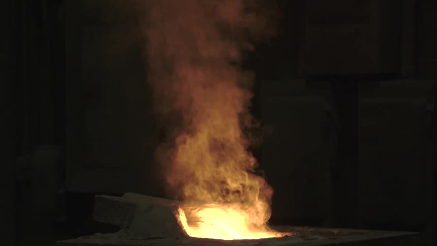 Thick orange smoke rises from a crucible of glowing molten metal in a dark foundry
