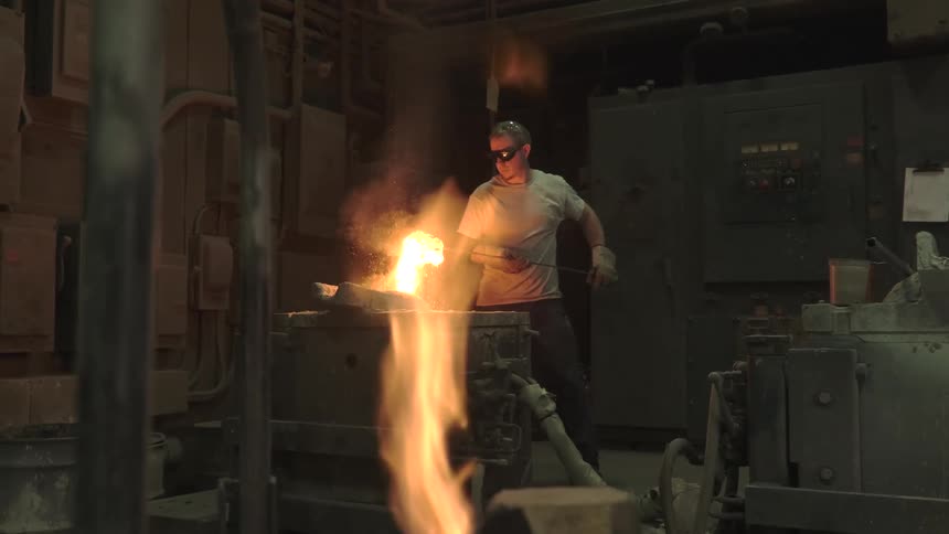 A foundry worker in protective gear handles a ladle of glowing molten metal, creating a fiery spectacle of sparks and smoke