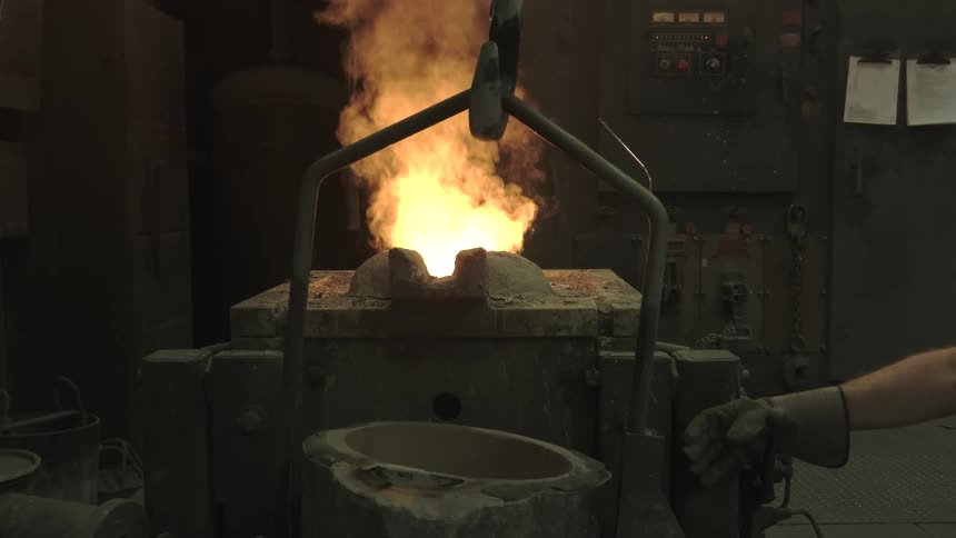 A crucible of molten metal burns with intense flames and smoke in a foundry in slow motion