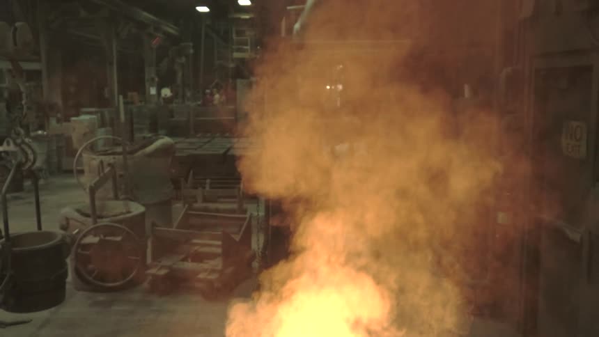 A fiery furnace glows intensely in a bustling industrial foundry as workers move in the background