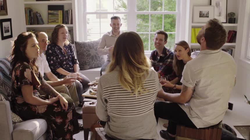 A group of friends laugh and talk as they sit in a living room