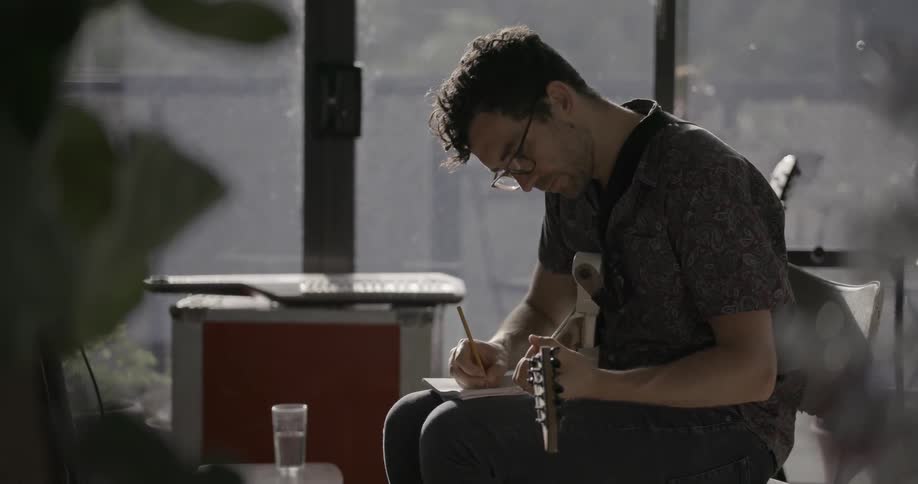 A man is sitting in his apartment playing guitar
